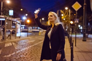 A young blonde woman is standing in the street waiting for an Uber ride.