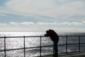 a grieving man leaning on a railing overlooking the ocean