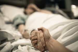 A Suffolk spinal cord injury lawyer holds the hand of an injured victim lying in a hospital bed.