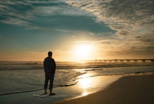 a man standing alone on a beach at sunrise